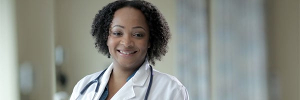 A medical assistant smiling at the camera in a coat and stethoscope