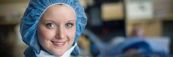 A smiling nurse with a blue hairnet and medical mask pulled down below her chin