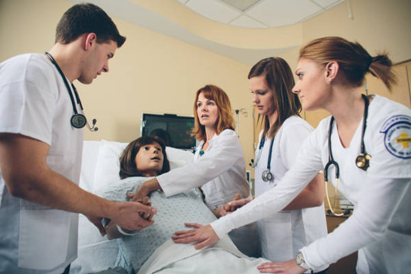 Four nursing students surrounding a simulation hospital bed with a high-tech dummy patient
