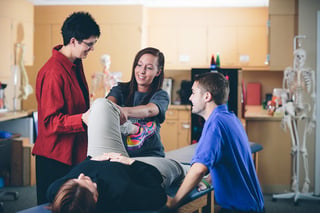 Physical Therapist Assistant students stretching out a volunteer in class with the professor's assistance