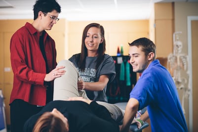 Physical therapist assistant students bending the knee of a volunteer who is laying down on their back