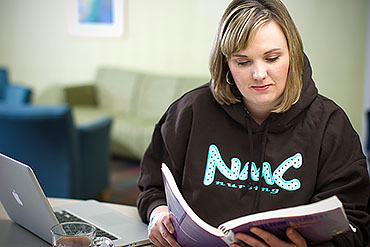 Transfer student studying her textbook while wearing an NMC Nursing hoodie