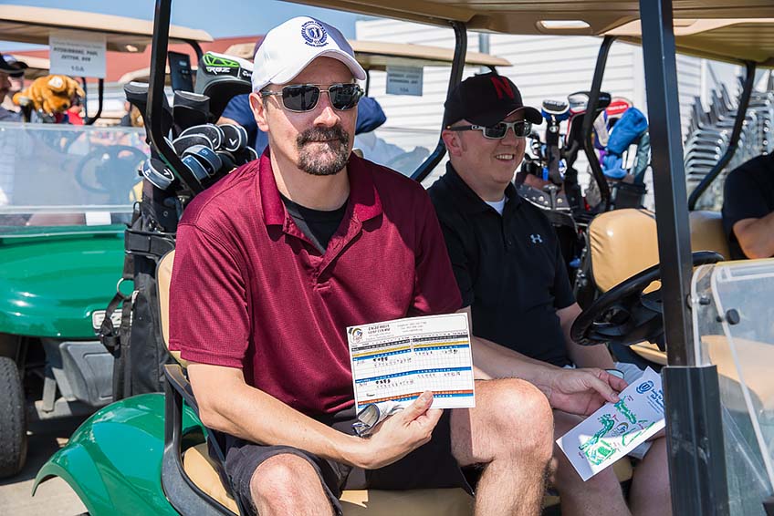 Matt Stockfeld in sunglasses and a hat, sitting in a golf cart, holding up his score card