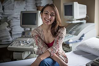 Felicia smiling and sitting on a bed near a myriad of sonography equipment