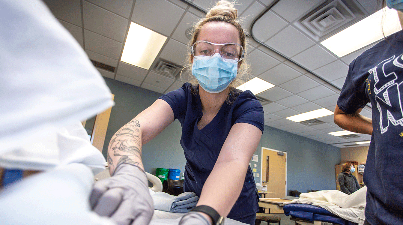 A student in the certified nursing assistant (CNA) program at Nebraska Methodist College practices preparing a bed for a patient.