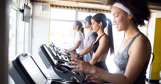 A group of four people lined up on their own treadmills, walking at a steady pace. In a medical fitness model, the focus is on creating exercise programs based on individual needs and wellness.