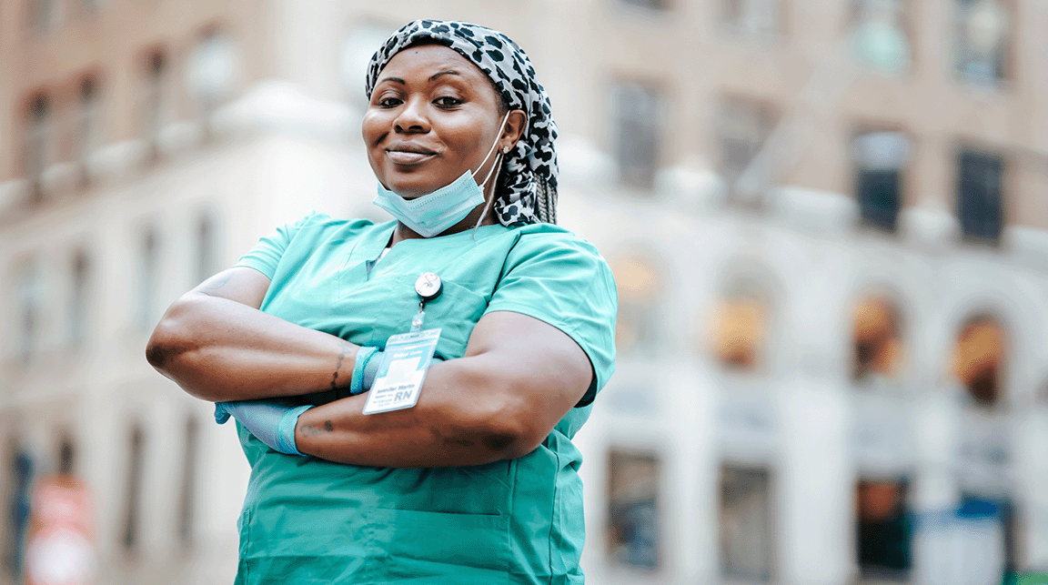 A nurse stands outside smiling with her arms folded across her chest.