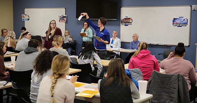 Associate professor Kiley Petersmith explains how the Poverty Simulation exercise works to NMC students.