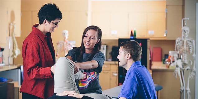 A physical therapist assistant working with a professor and classmate to learn how to stretch out the knee of a volunteer. A physical therapist assistant program can be a natural step for exercise science majors.