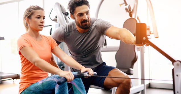 A wellness coach in a facility works to promote medical fitness with a client as she uses one of the exercise machines.