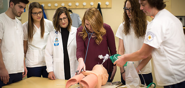 Respiratory therapy instructor and students surround a medical dummy, applying the lessons they are learning in their respiratory care courses