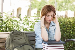 A stressed student resting her elbows on a stack of textbooks and massaging her temples