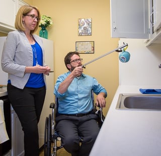 An occupational therapist with a patient in a wheelchair using an extender to reach things in high places. Occupational therapists help patients with the skills they need to do, want to do and have to do to enjoy a meaningful life. 