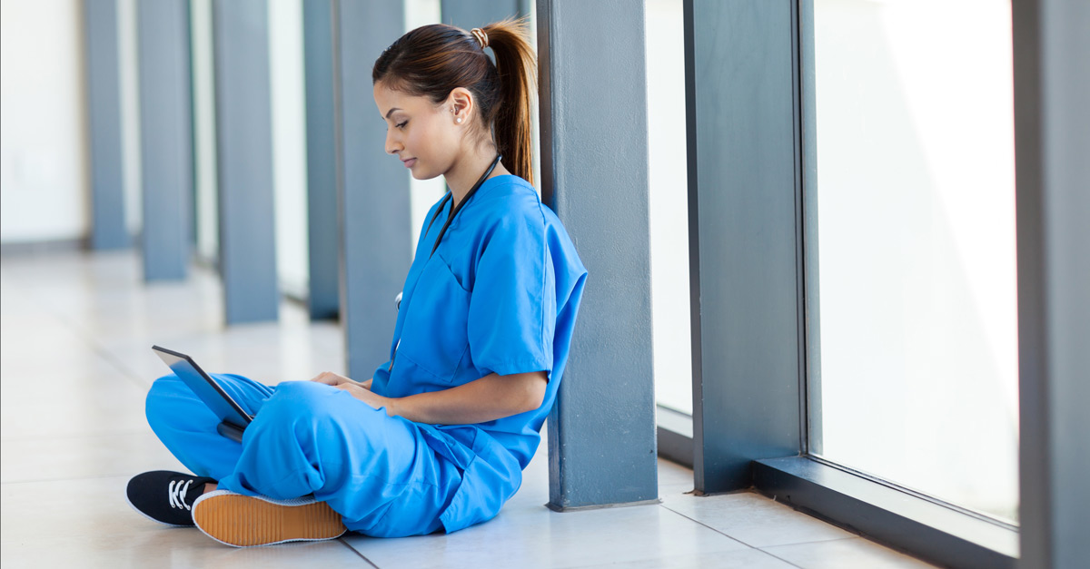 Nurse in scrubs sits with laptop to study for RN to BSN online.