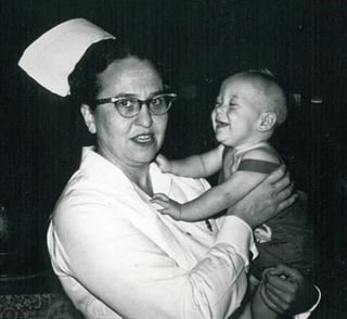 Miss Fagan in her nurse's uniform, holding a smiling toddler
