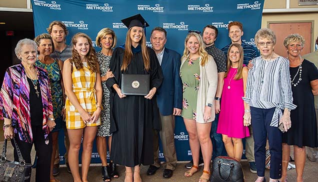 New NMC MOT graduate Megan Vermeer holding her diploma and surrounded by family members.