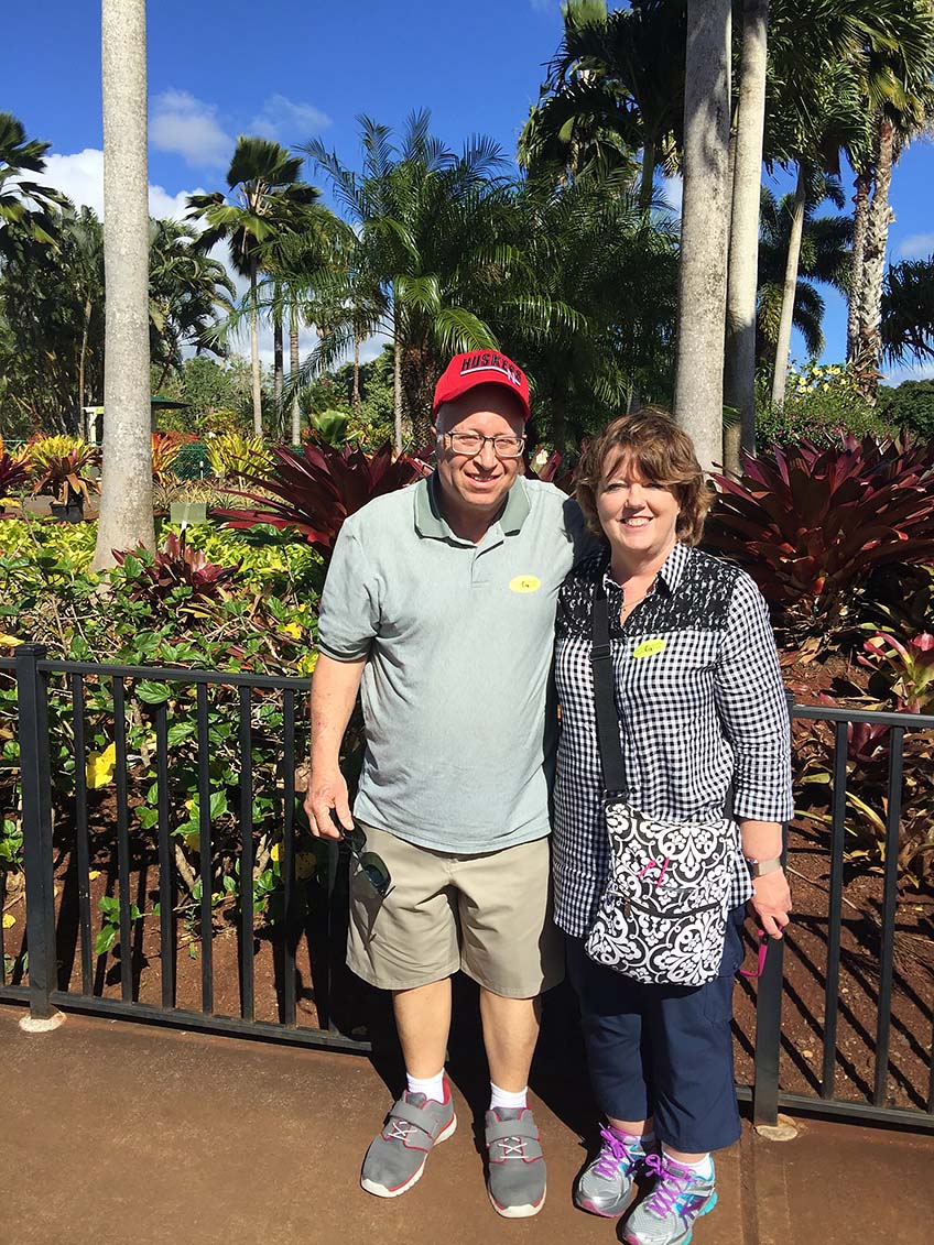 Peggy Dyer posing with her husband in front of palm trees on vacation