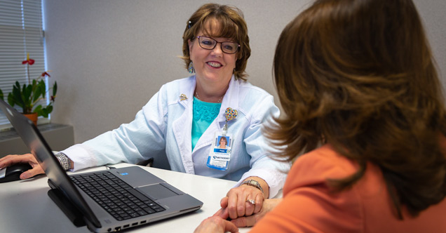 Peggy Dyer working with a patient, holding the patients hand and smiling at her