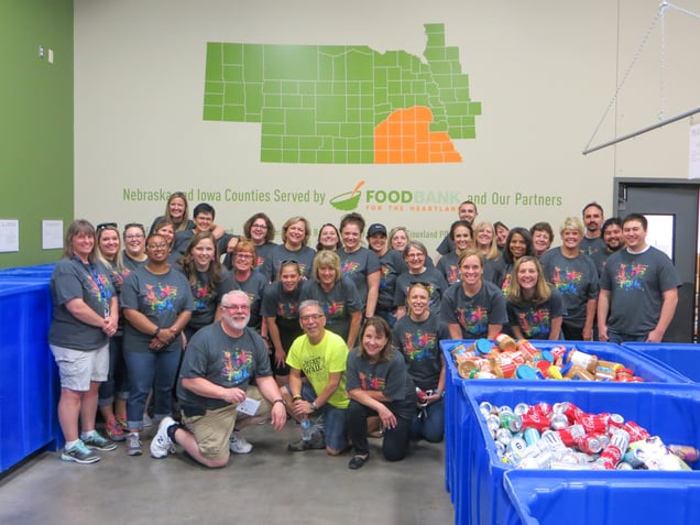Nebraska Methodist College staff and faculty wearing matching shirts, all standing in front of the wall at the food bank that features a graphic of their service area in Nebraska and Iowa