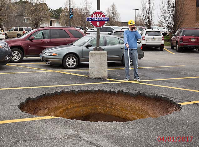A construction worker on his phone in the NMC parking lot, standing in front of a 15 ft wide hole in the parking lot