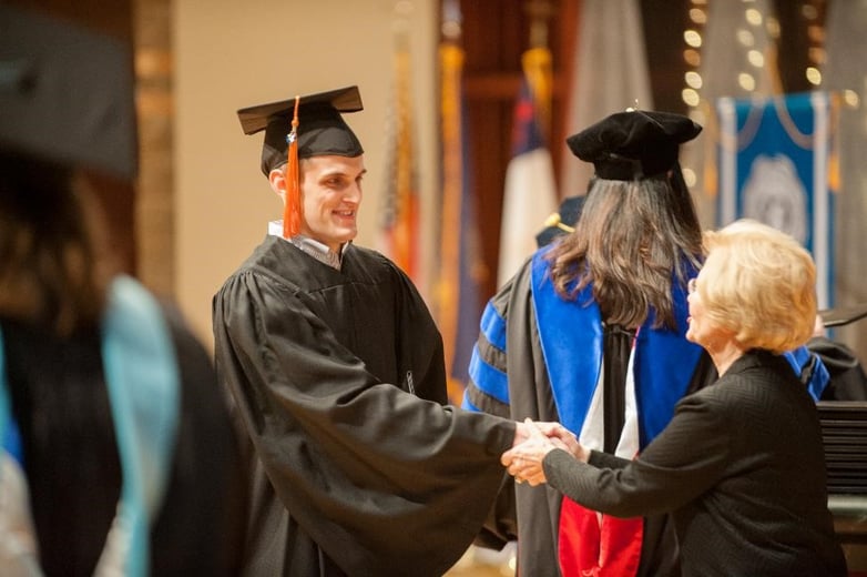 A man in his cap and gown shaking a member of the nursing college's faculty, before being handed his bachelor of science in nursing (BSN) degree