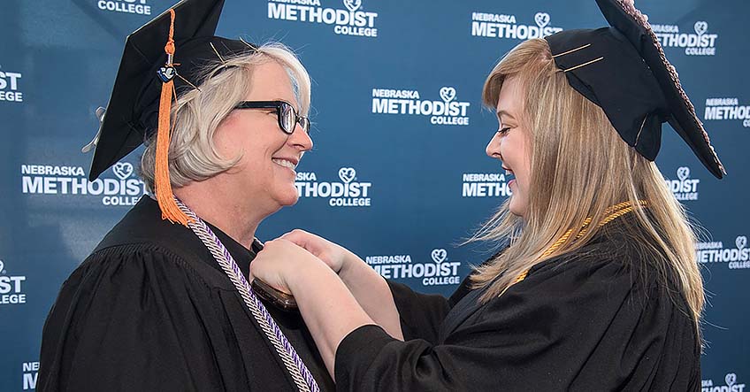 Lisa Kessler smiles as her daughter, Cassandra, helps adjust Lisa's graduation gown.