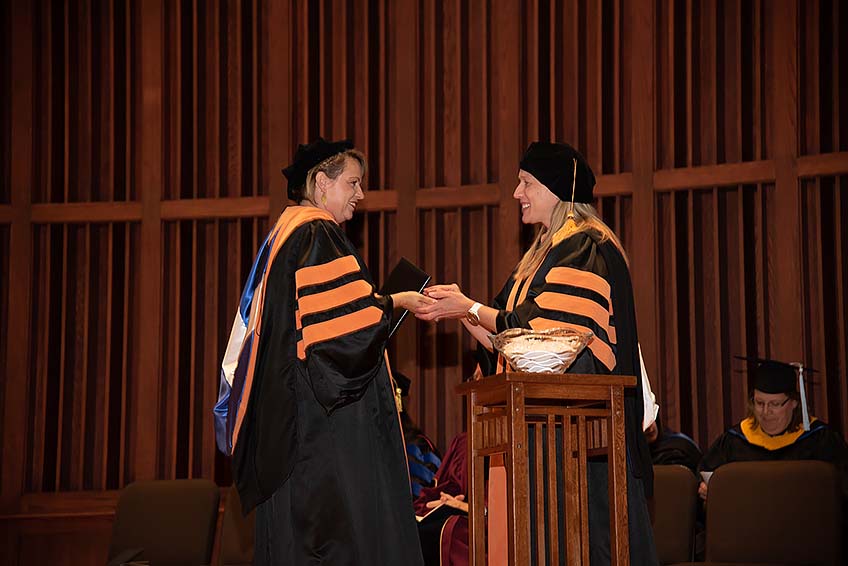 Faculty member Jillian Krumbach congratulates a graduate and hands her a starfish, a special tradition from the alumni department.