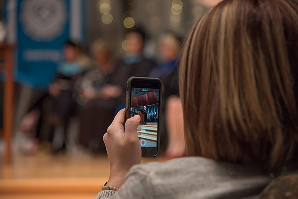 Cassandra holds up her iPhone, recording a video of Lisa's commencement address