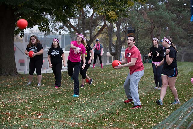 Students in the grass on campus throwing dodgeballs at an opposing team